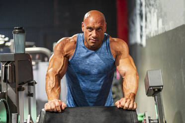 Bald bodybuilder leaning on exercise machine in gym - DLTSF03010