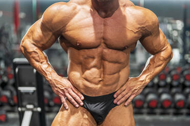 Muskulöser Bodybuilder mit angewinkelten Armen, der seine Bauchmuskeln im Fitnessstudio beugt - DLTSF03019