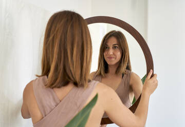 Smiling woman looking in mirror at home - VEGF05747