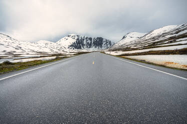 Norwegen, Innlandet, Norwegische Nationalstraße 15, die sich zwischen schneebedeckten Hügeln erstreckt - RJF00925