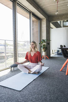 Geschäftsfrau macht Yoga im Schneidersitz auf einer Übungsmatte im Büro - UUF26896