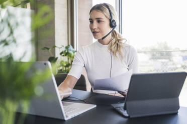 Customer service representative wearing headset working on laptop in office - UUF26903