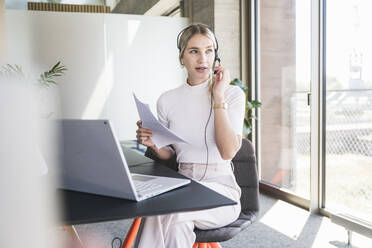 Young customer service representative talking on headset sitting at desk in office - UUF26906