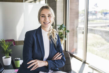 Happy businesswoman with arms crossed in office - UUF26917