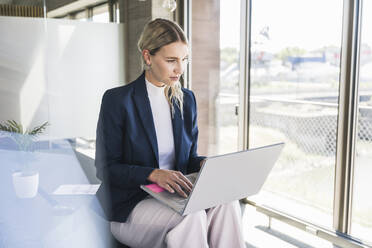 Businesswoman wearing blazer working on laptop in office - UUF26918