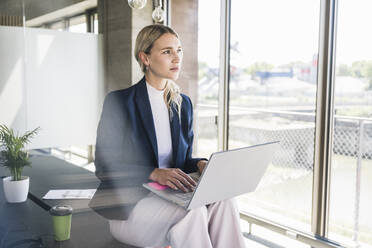 Nachdenkliche Geschäftsfrau mit Laptop auf dem Schreibtisch im Büro - UUF26919