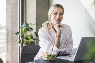 Smiling doctor with hand on chin sitting at desk - UUF26943