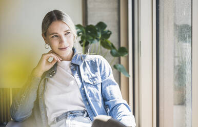 Junge Geschäftsfrau in Jeansjacke sitzt an einem sonnigen Tag im Büro - UUF26945