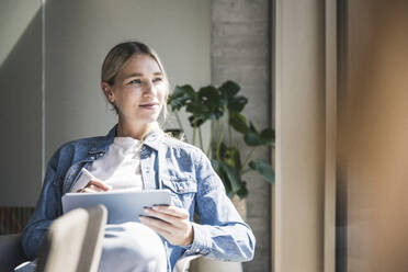 Contemplative businesswoman with tablet PC sitting in office - UUF26947