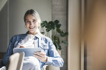 Happy businesswoman with tablet PC in office - UUF26948