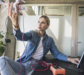 Woman analyzing drone sitting at desk in office - UUF26951