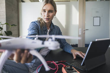 Woman examining drone using tablet PC at office - UUF26952