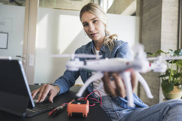 Blond woman holding drone using tablet PC in office - UUF26953