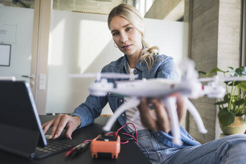 Blonde Frau mit Drohne und Tablet-PC im Büro - UUF26953