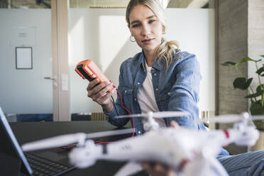 Woman measuring voltage of drone through multimeter in office - UUF26954