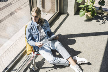 Businesswoman sitting on floor with tablet PC and wind turbine model in office - UUF26957