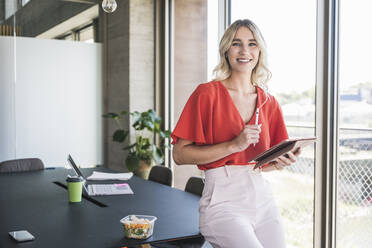 Blond businesswoman with digitized pen and tablet PC in office - UUF26968