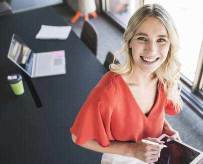 Happy blond businesswoman holding tablet PC in office - UUF26970
