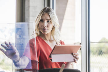 Geschäftsfrau hält Tablet-PC und berührt transparenten Bildschirm im Büro - UUF26981