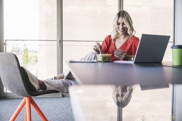 Businesswoman having lunch using smart phone sitting at desk in office - UUF26985