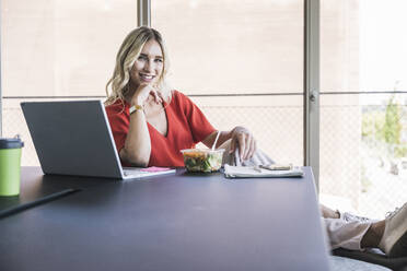 Geschäftsfrau sitzt mit Laptop und Lunchpaket am Schreibtisch im Büro - UUF26988