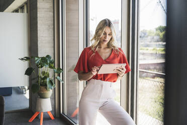 Blonde Geschäftsfrau mit Tablet-PC am Fenster im Büro - UUF26992