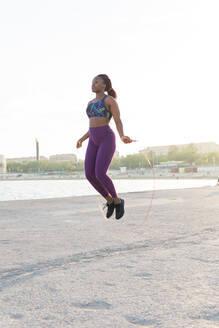 Ganzkörper fit schwarze Frau Athleten in Sportkleidung Springen mit Seil am Meer Ufer - ADSF35946