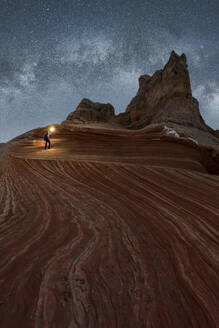 Silhouette eines nicht erkennbaren Forschers, der mit einer Taschenlampe auf einer Landschaft von Felsformationen im Hochland unter einem milchigen Sternenhimmel im Vermillion Cliffs National Monument, Arizona in den USA steht - ADSF36054