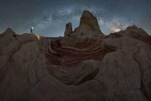 Silhouette eines nicht erkennbaren Forschers, der mit einer Taschenlampe auf einer Landschaft von Felsformationen im Hochland unter einem milchigen Sternenhimmel im Vermillion Cliffs National Monument, Arizona in den USA steht - ADSF36055