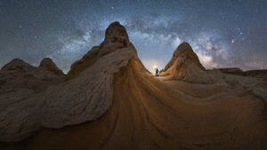 Silhouette eines nicht erkennbaren Forschers, der mit einer Taschenlampe auf einer Landschaft von Felsformationen im Hochland unter einem milchigen Sternenhimmel im Vermillion Cliffs National Monument, Arizona in den USA steht - ADSF36056