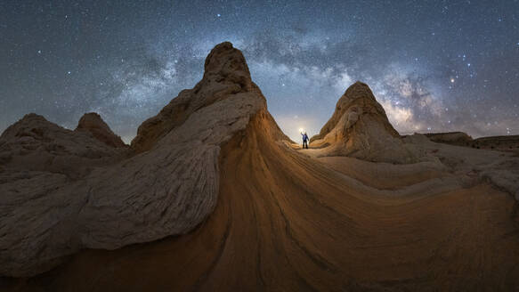 Silhouette eines nicht erkennbaren Forschers, der mit einer Taschenlampe auf einer Landschaft von Felsformationen im Hochland unter einem milchigen Sternenhimmel im Vermillion Cliffs National Monument, Arizona in den USA steht - ADSF36056