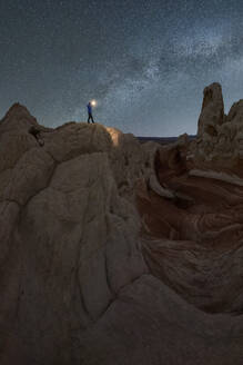 Silhouette eines nicht erkennbaren Forschers, der mit einer Taschenlampe auf einer Landschaft von Felsformationen im Hochland unter einem milchigen Sternenhimmel im Vermillion Cliffs National Monument, Arizona in den USA steht - ADSF36058