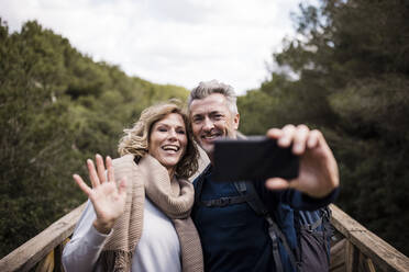 Happy mature man with woman waving hand at smart phone - JOSEF11284