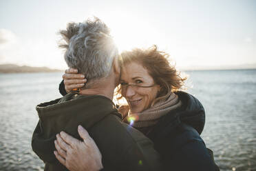 Lächelnde reife Frau umarmt Mann am Strand an einem sonnigen Tag - JOSEF11296