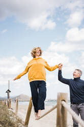 Glückliche Frau hält Hand mit Mann, der an einem Seil am Strand spazieren geht - JOSEF11302