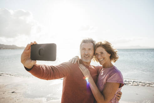 Glückliche reife Frau mit Mann nimmt Selfie durch Smartphone am Strand - JOSEF11310