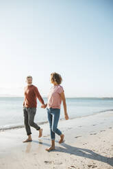 Älterer Mann und Frau halten sich an den Händen und gehen am Strand spazieren - JOSEF11321