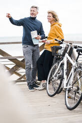 Glücklicher Mann mit Frau neben einem Fahrrad am Strand stehend - JOSEF11323