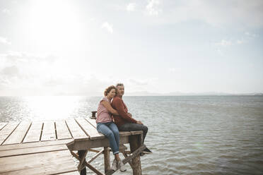 Mature couple sitting on jetty over sea - JOSEF11329