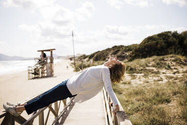 Active mature woman balancing on boardwalk at beach - JOSEF11346