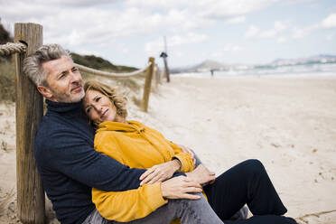 Lächelnde reife Frau mit Mann, der sich am Strand auf einen Pfahl stützt - JOSEF11360