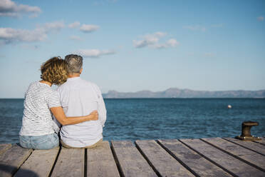 Mature couple spending time together sitting on jetty looking at sea - JOSEF11363