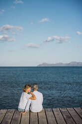 Mature woman with man sitting on jetty looking at sea - JOSEF11365