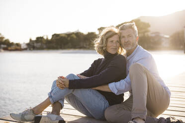 Happy mature couple sitting on jetty at sunny day - JOSEF11367