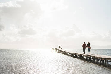 Mature couple holding hands walking on jetty over sea - JOSEF11391
