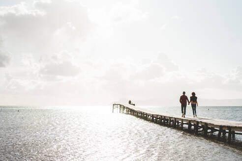 Mature couple holding hands walking on jetty over sea - JOSEF11391