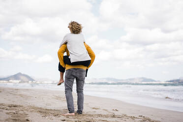 Man giving piggyback ride to woman on shore at beach - JOSEF11406