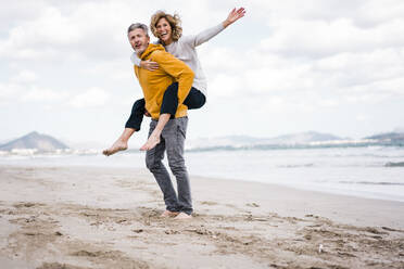 Reifer Mann mit Frau genießt Huckepackfahrt am Strand - JOSEF11408