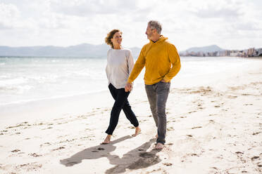 Lächelnde Frau und Mann halten sich an den Händen und gehen am Strand spazieren - JOSEF11411