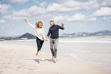 Cheerful mature couple having fun on shore at beach - JOSEF11419